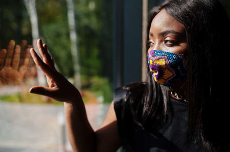 Fashionable african american woman, wear hand made face mask stand against window.