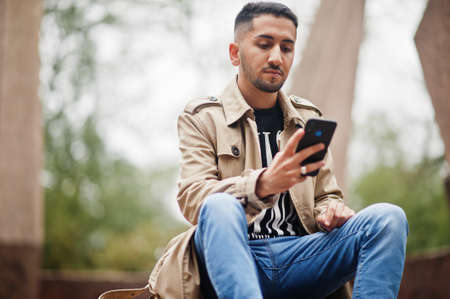 Stylish kuwaiti man at trench coat with mobile phone.