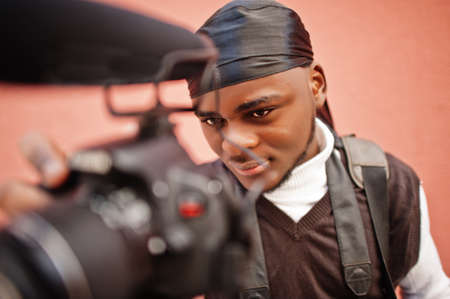 Young professional african american videographer holding professional camera with pro equipment....