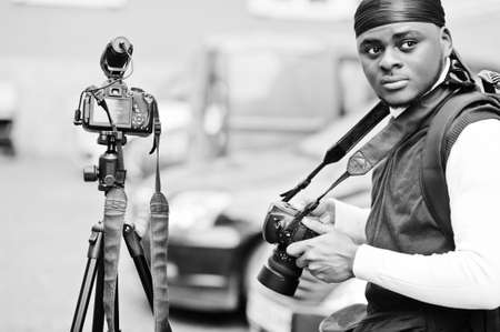 Young professional african american videographer holding professional camera with tripod pro...