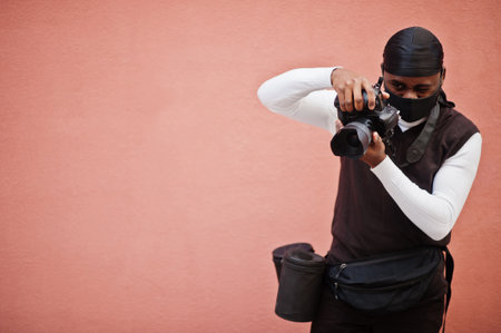 Young professional african american videographer holding professional camera with pro equipment. Afro cameraman wearing black duraq and face protect mask, making a videos.の写真素材
