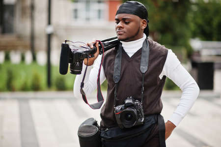 Young professional african american videographer holding professional camera with pro equipment....