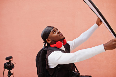 Young professional african american videographer holding professional camera with pro equipment. Afro cameraman wearing black duraq making a videos.の写真素材