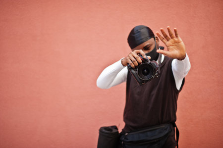 Young professional african american videographer holding professional camera with pro equipment. Afro cameraman wearing black duraq and face protect mask, making a videos.の写真素材