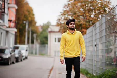 Urban young hipster indian man in a fashionable yellow sweatshirt. Cool south asian guy wear hoodie walking on fall street.の写真素材
