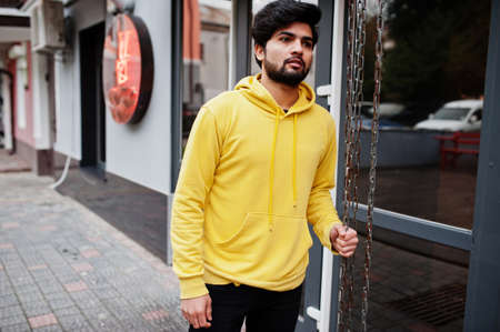 Urban young hipster indian man in a fashionable yellow sweatshirt. Cool south asian guy wear hoodie.