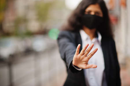 Gorgeous indian woman wear formal and black face mask, posing at street during covid pandemia. She show stop sign by hand.の写真素材