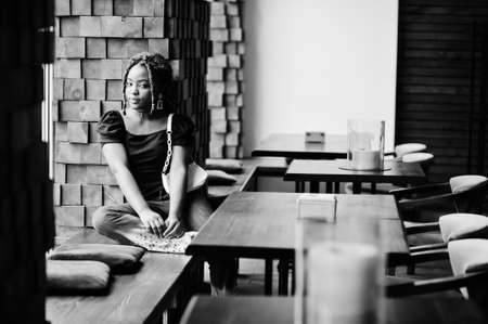 Lovely african american woman with dreadlocks in blue stylish jeans at cafe. Beautiful cool fashionable black young girl indoor.の写真素材