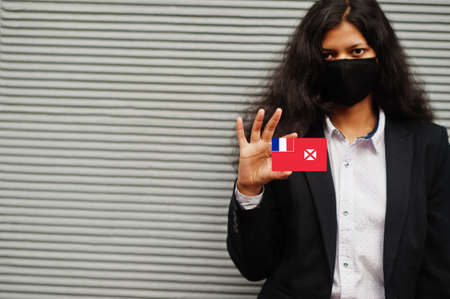 Asian woman at formal wear and black protect face mask hold Wallis and Futuna flag at hand against gray background. Coronavirus at country concept.の写真素材