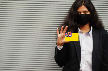 Asian woman at formal wear and black protect face mask hold Niue flag at hand against gray...