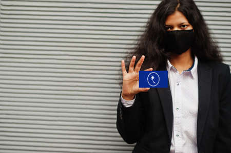 Asian woman at formal wear and black protect face mask hold Chuuk State flag at hand against gray...