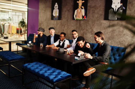 Group of handsome retro well-dressed man gangsters spend time at club, sitting and drinking whiskey. Multiethnic male bachelor mafia party in restaurant.の写真素材