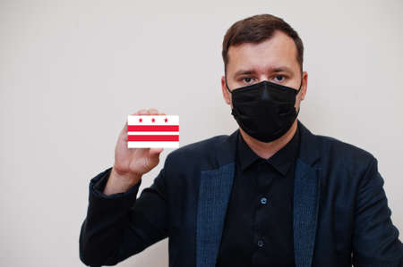 Man wear black formal and protect face mask, hold District of Columbia flag card isolated on white...