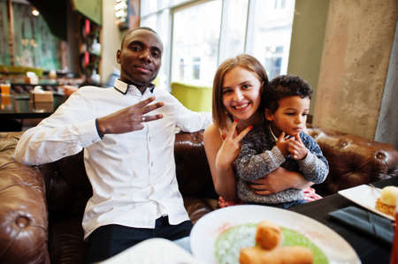 Happy multiethnic family with boy kid spend time at restaurant. Relationships of african man and white european woman.の写真素材