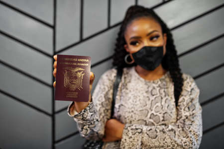 African american woman wearing black face mask show Ecuador passport in hand. Coronavirus in America...
