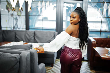 Beautiful african american woman in white blouse and red leather pants pose at restaurant.の写真素材