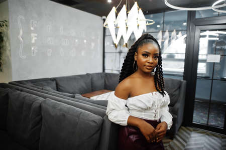 Beautiful african american woman in white blouse and red leather pants pose at restaurant.