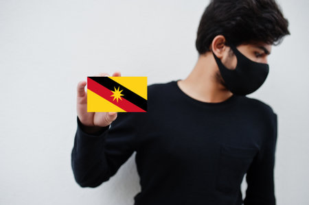 Malay man wear all black with face mask hold Sarawak flag in hand isolated on white background. States and federal territories of Malaysia coronavirus country concept.の写真素材