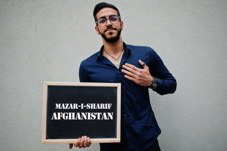Arab man wear blue shirt and eyeglasses hold board with Mazar-i-Sharif Afghanistan inscription. Largest cities in islamic world concept.の写真素材