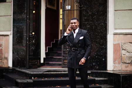 Portrait of young and handsome african american businessman in suit speak on mobile phone, prepare for meeting.の写真素材