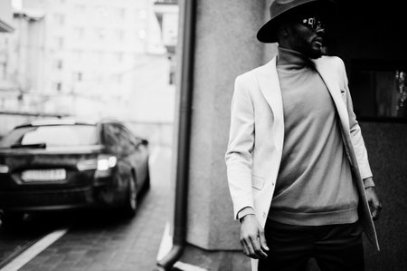 Stylish african american man wear beige jacket and black hat with sunglasses pose near car.の写真素材