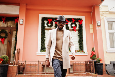 Stylish african american man wear beige jacket and black hat with sunglasses pose against house with new year decorations and wreath.の写真素材