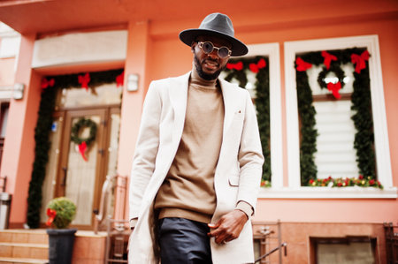 Stylish african american man wear beige jacket and black hat with sunglasses pose against house with new year decorations and wreath.の写真素材