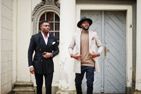 Two fashion black men walking on street. Fashionable portrait of african american male models. Wear suit, coat and hat.の写真素材