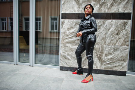 Fashionable beautiful african american woman posing in black leather jacket and pants at street.