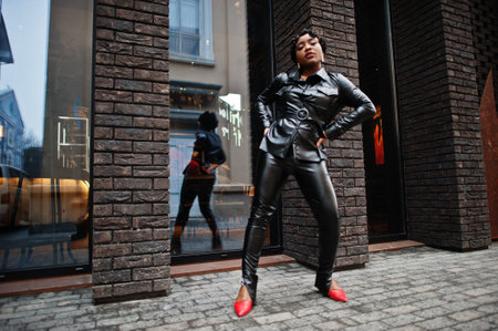 Fashionable beautiful african american woman posing in black leather jacket and pants at street.の写真素材
