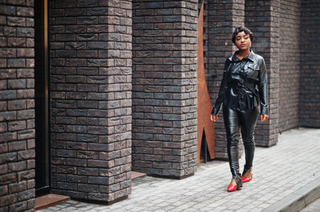 Fashionable beautiful african american woman posing in black leather jacket and pants at street.の写真素材