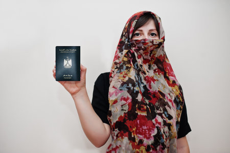 Young arabian muslim woman in hijab clothes hold Arab Republic of Egypt passport on white wall background, studio portrait.の写真素材