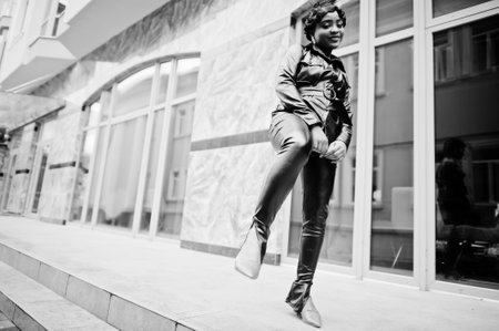 Fashionable beautiful african american woman posing in black leather jacket and pants at street.の写真素材