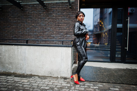 Fashionable beautiful african american woman posing in black leather jacket and pants at street.の写真素材
