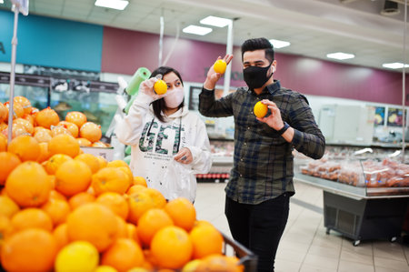 Asian couple wear in protective face mask shopping together in supermarket during pandemic. Choosing different fruits.の写真素材