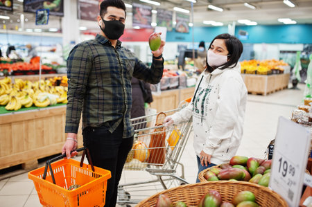 Asian couple wear in protective face mask shopping together in supermarket during pandemic. Taking...