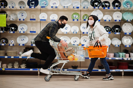 Asian couple wear in protective face mask shopping together in supermarket during pandemic. Having fun with shopping cart.の写真素材