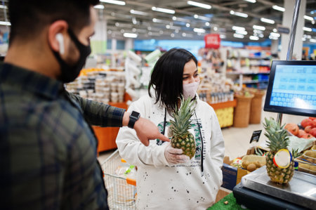 Asian couple wear in protective face mask shopping together in supermarket during pandemic. Weigh...