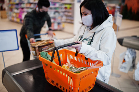 Asian couple wear in protective face mask shopping together in supermarket during pandemic. On the cash register.の写真素材