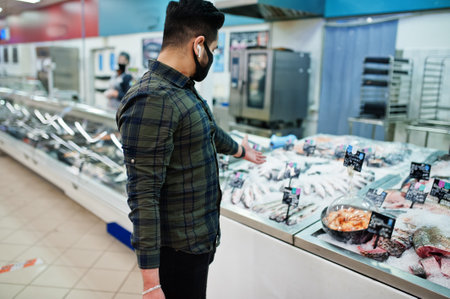 Asian man wear in protective face mask shopping in supermarket during pandemic. Choose seafood.の写真素材