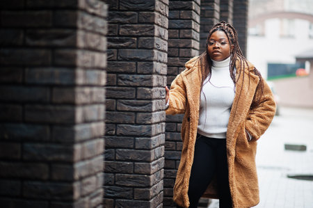 Glamorous african american woman in warm fur coat, eyeglasses pose at street.