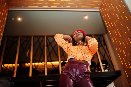 Elegant afro american woman in red french beret, big gold neck chain polka dot blouse and leather pants pose indoor.の写真素材