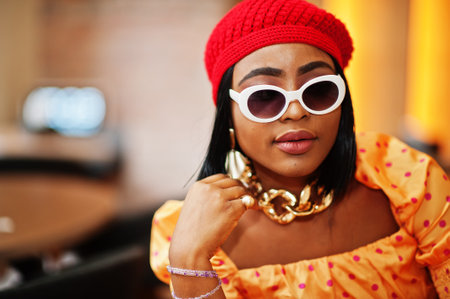 Elegant afro american woman in red french beret, big gold neck chain, sunglasses, polka dot blouse pose indoor.の写真素材