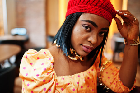 Elegant afro american woman in red french beret, big gold neck chain polka dot blouse pose indoor.