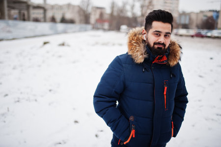 Beard indian man wear jacket in cold winter day. Mobile earphones in ears.