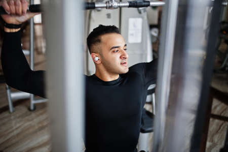 Muscular arab man training and doing workout on fitness machine in modern gym.