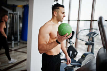Muscular arab man training in modern gym. Fitness arabian men with naked torso doing exercises with ball.の写真素材