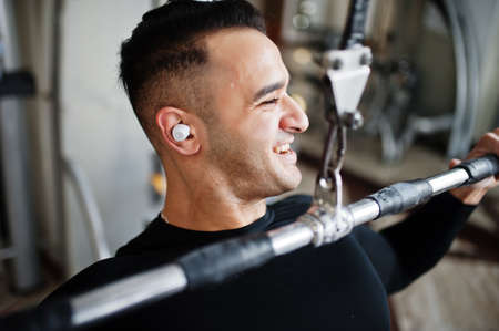 Muscular arab man training and doing workout on fitness machine in modern gym.