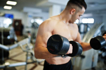 Muscular arab man training in with dumbbells modern gym. Fitness arabian men with naked torso doing...