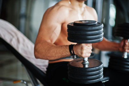 Muscular arab man training in with dumbbells modern gym. Fitness arabian men with naked torso doing workout.の写真素材